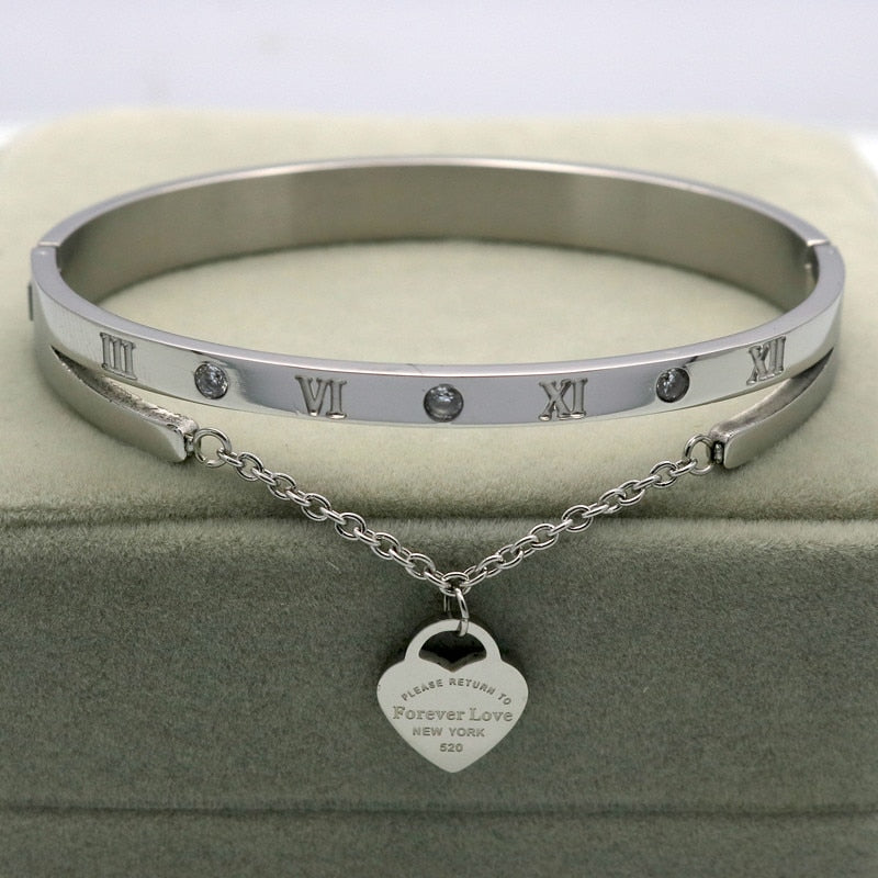 Delight in this timeless classic a Hanging Heart Label Forever Love Bracelet! Crafted of gleaming stainless steel, its Heart shape/pattern and bangle design add exquisite beauty to any look. An ideal accessory for any woman!